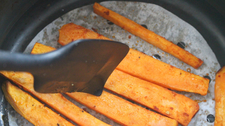 sweet potato spears in air fryer basket with spatula