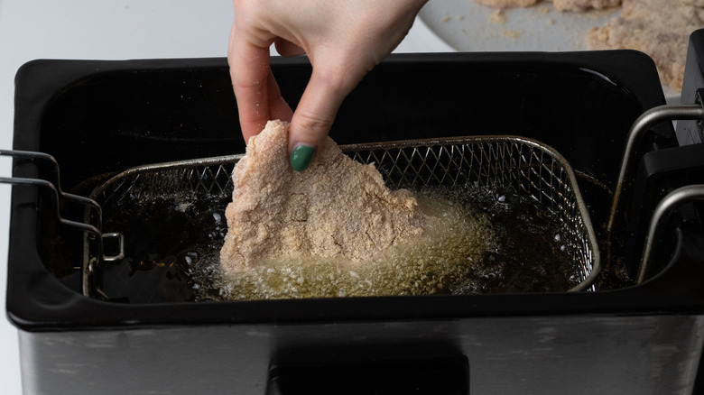 hand placing chicken in fryer