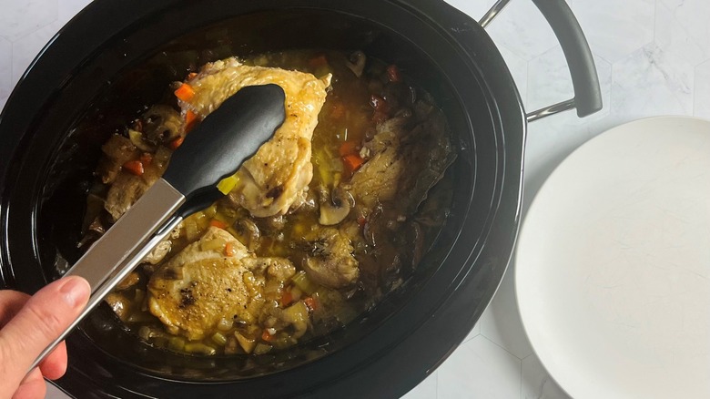 Chicken thighs being removed from a crock pot