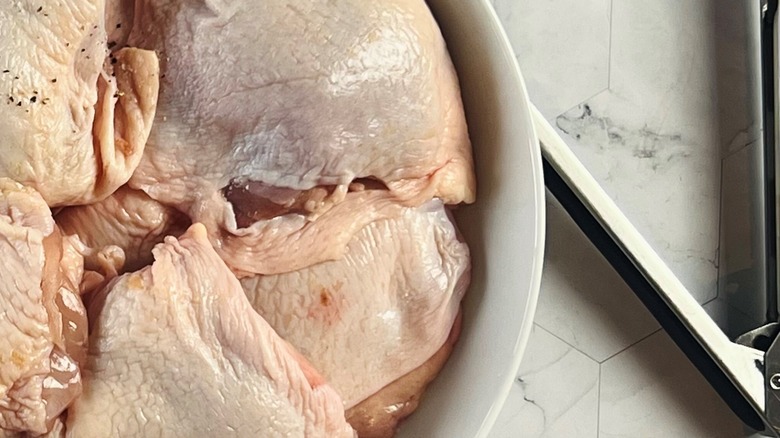 Salt and pepper being poured over chicken thighs