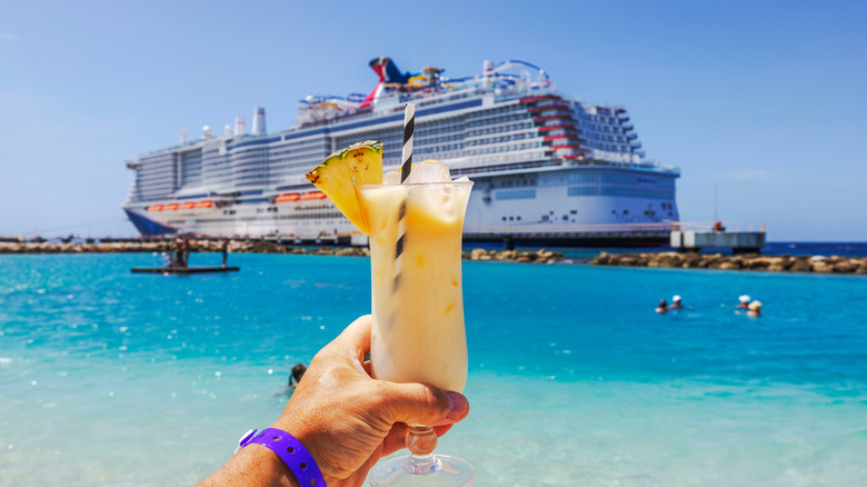 person holding a cocktail from the beach with a cruise ship in the background