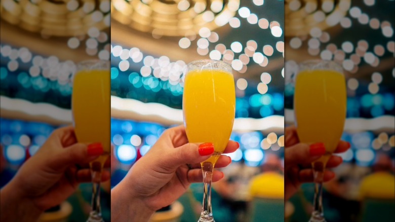 woman's hand holding a mimosa in the atrium of a Carnival cruise ship