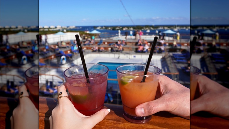 two people holding cocktails while overlooking the pool on a Margaritaville ship