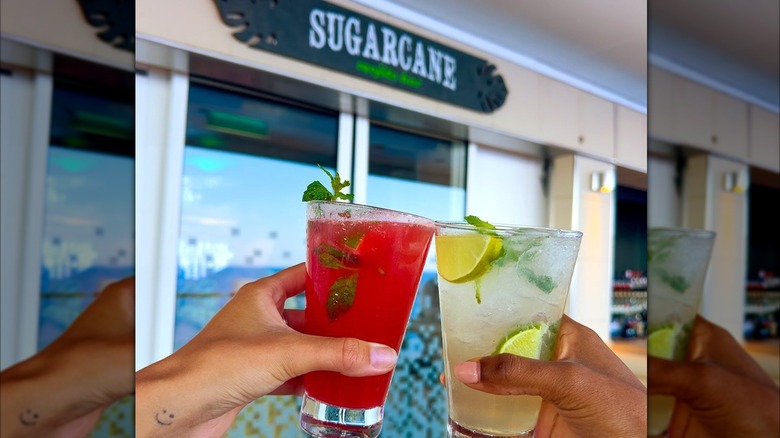 two people holding up cocktails in front of the Sugarcane bar on Norwegian Cruise Line