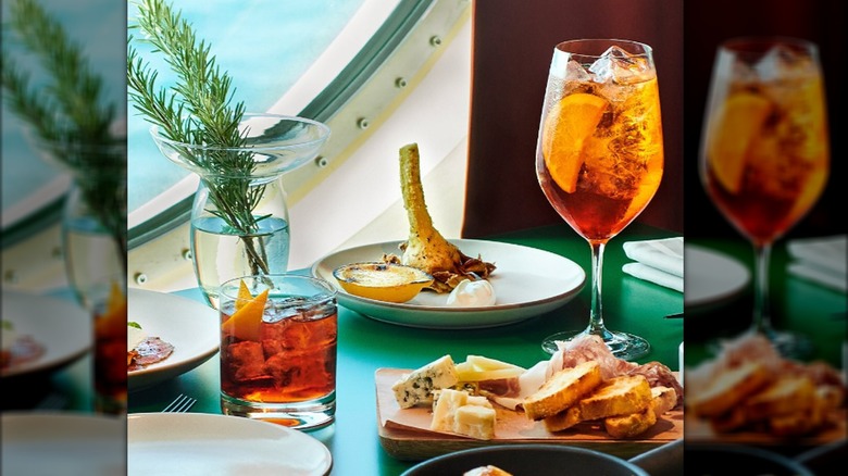 two cocktails on a table along with multiple plates of food on Virgin Voyages