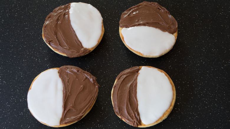 Four black and white cookies on black speckled surface