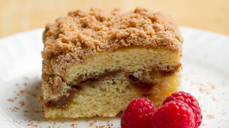 A slice of crumb cake with raspberries on a white plate