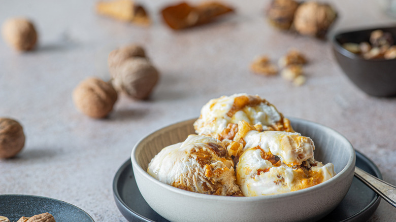 Three scoops of maple walnut ice cream in a dish surrounded by shell walnuts