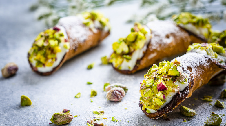 Three pistachio cannoli laid on surface surrounded by pistachio pieces