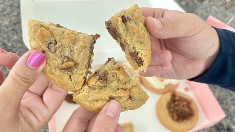 Three hands holding up Crumbl chocolate chip cookie quarter pieces