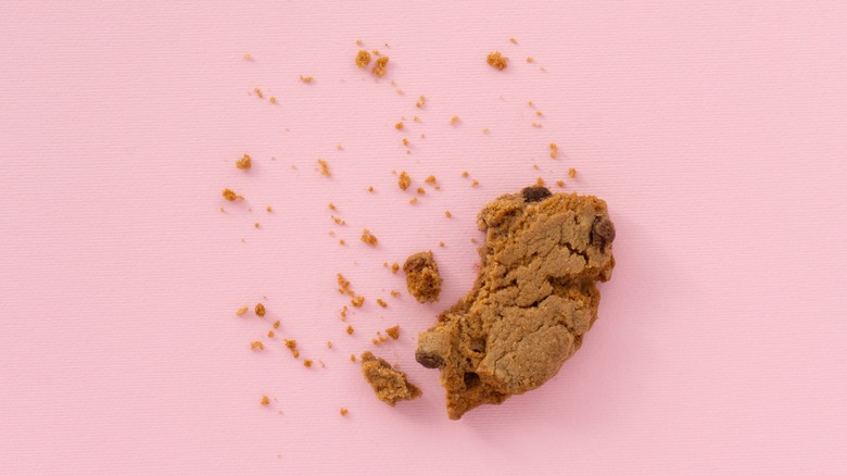 A chocolate chip cookie piece with crumbs on pink background