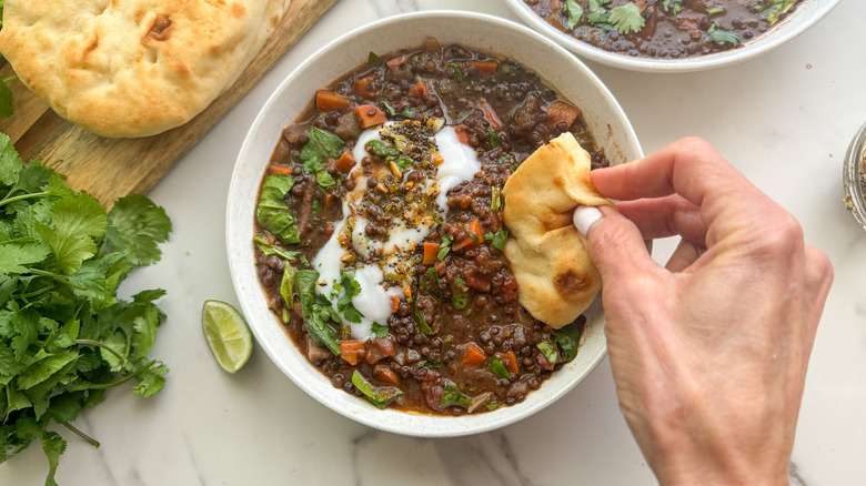 hand dipping naan in soup