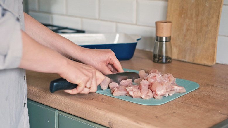 Hands slicing chicken on a cutting board