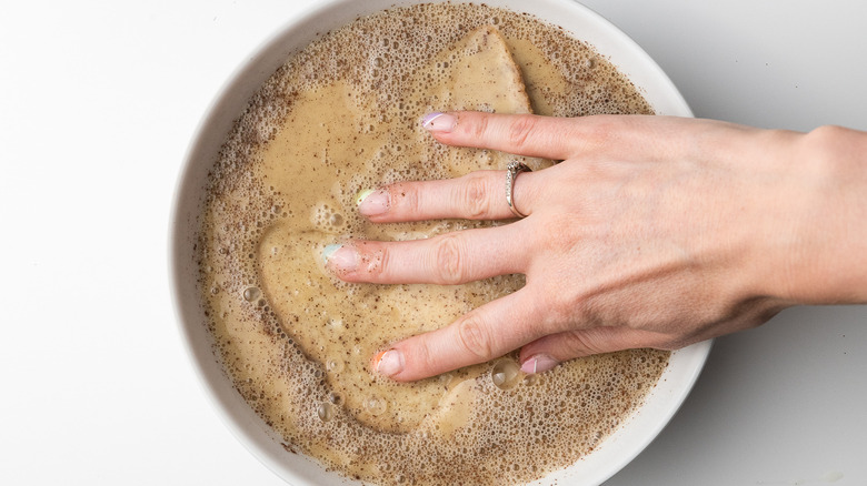 hand dipping bread in batter 