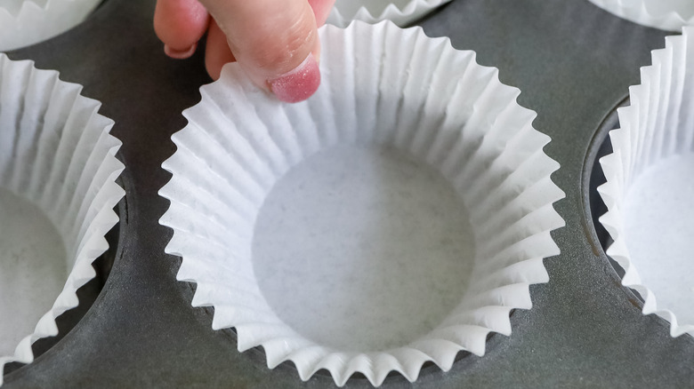 muffin liners being put into a muffin tin