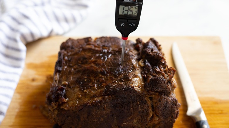 prime rib on a wooden cutting board with a meat thermometer in it