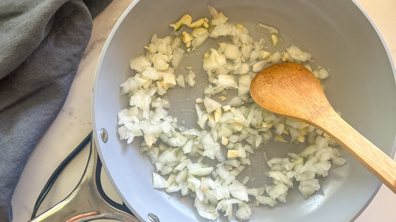 wooden spoon stirring diced onion in pan