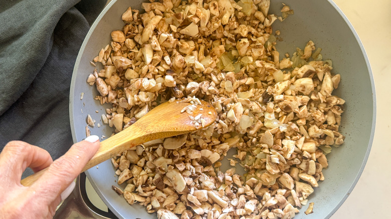 wooden spoon stirring chopped mushrooms in pan