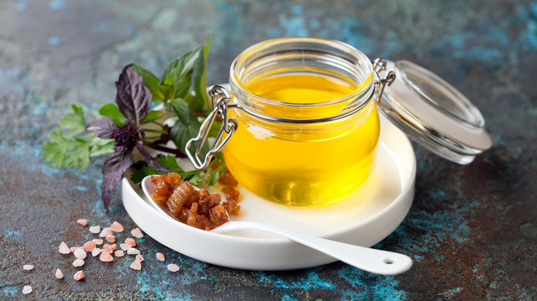a jar of duck fat sitting on a white plate next to a spoon with bits of duck skin on it