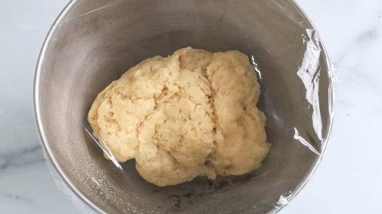 Beignet dough in a bowl covered with plastic wrap