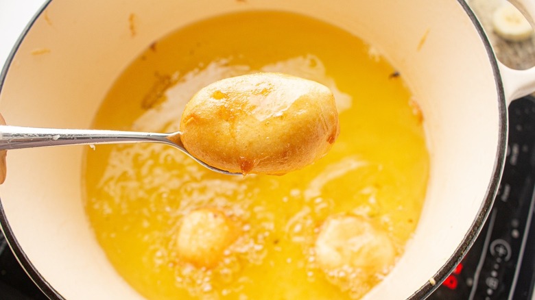 Spoon holding fried banana over pot