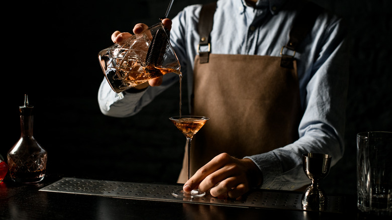 mixologist pouring brown liquor into martini glass