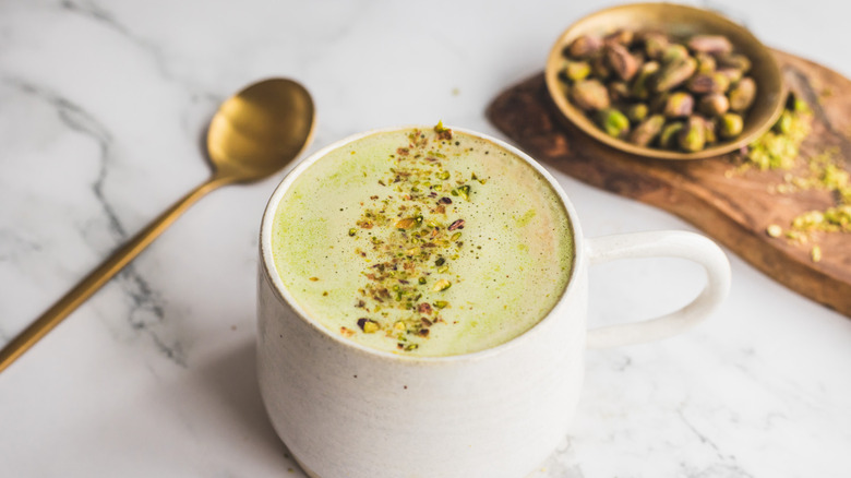 white cup of pistachio latte with golden spoon and pistachios