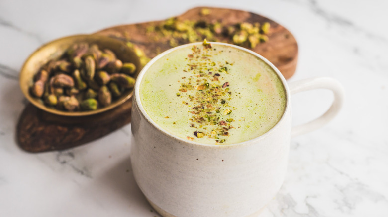 white cup of pistachio latte with pistachios on board