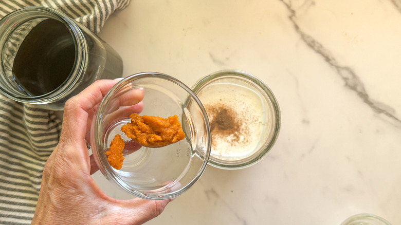 hand adding pumpkin to jar