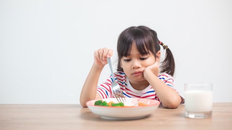 unhappy child at table with plate of food