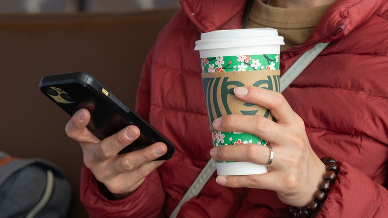 Close-up of a person holding a Starbucks drink and smart phone