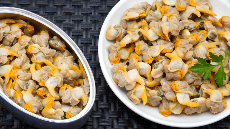 A tin of canned clams and next to canned clams plated with parsley