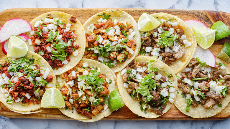 Mexican street tacos on a wood tray on a marble background