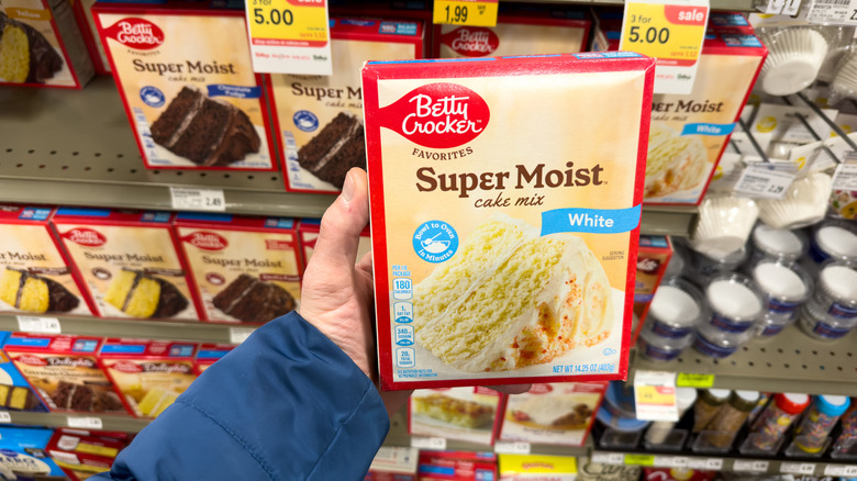 Grocery shopper holding a box of dry cake mix in a supermarket aisle