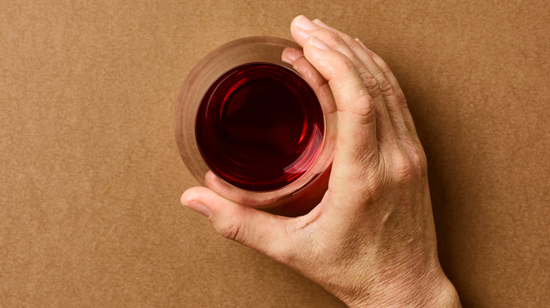 Top-down view of a hand gripping a stemless glass full of red wine