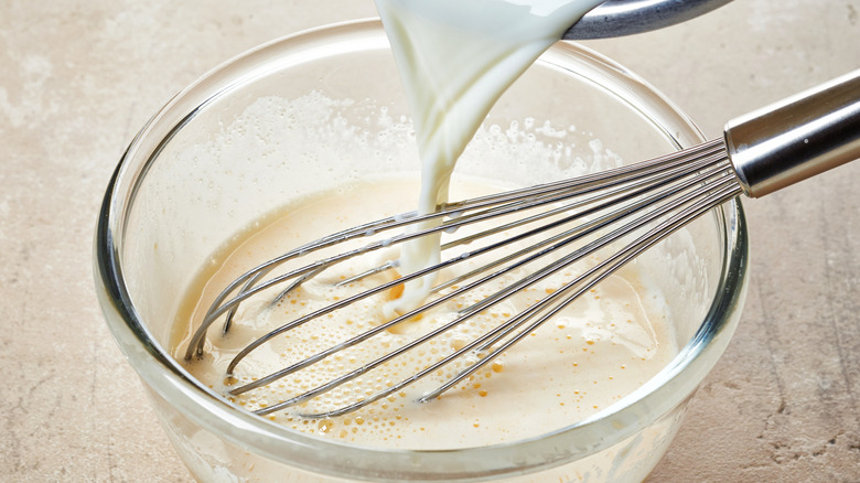 Pouring and whipping milk into an egg mix in a glass bowl