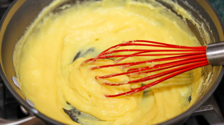 Whisking pastry cream in pot with a red silicon whisk