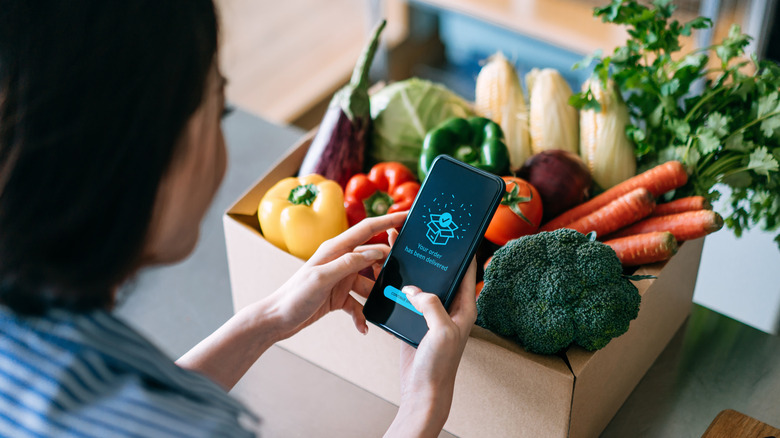 Woman with phone and box of veggies