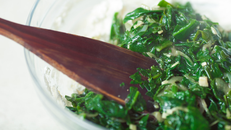 cooked spinach in a glass bowl with wooden spoon