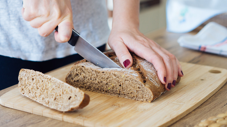 Hands slicing bread on cutting board