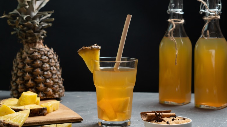 pinapple tepache in a glass with bottles and whole pineapple in the background