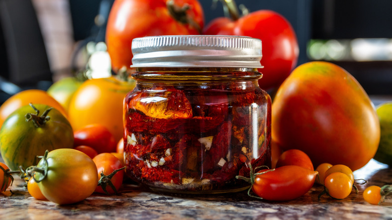 Ripe tomatoes piled behind jar of sun-dried tomatoes in oil