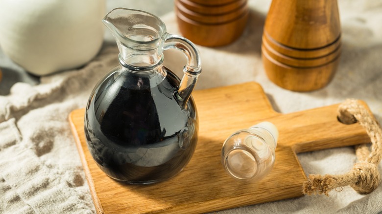 A pitcher of balsamic reduction on a wooden board