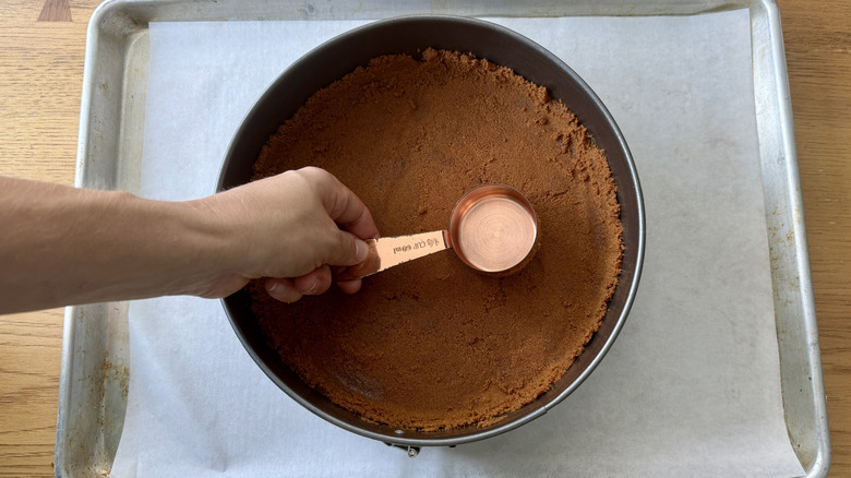 measuring cup pressing crust into pan