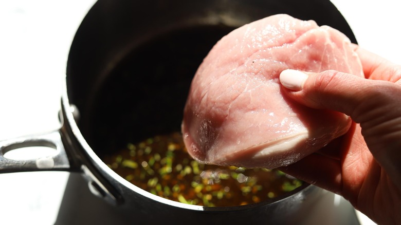 Raw pork chops being placed in marinade