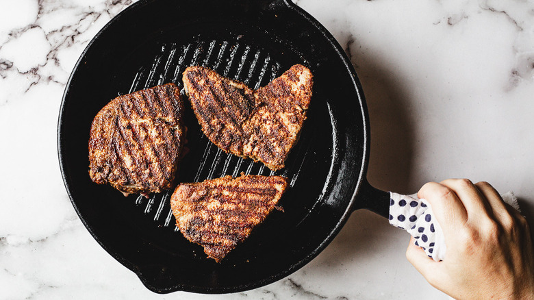 Hand holding tuna steaks in grill pan