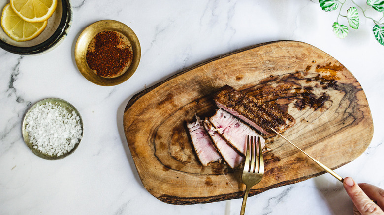 Slicing tuna on a cutting board surrounded by sauce