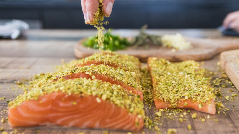 Person sprinkling dry seasoning over raw salmon filets