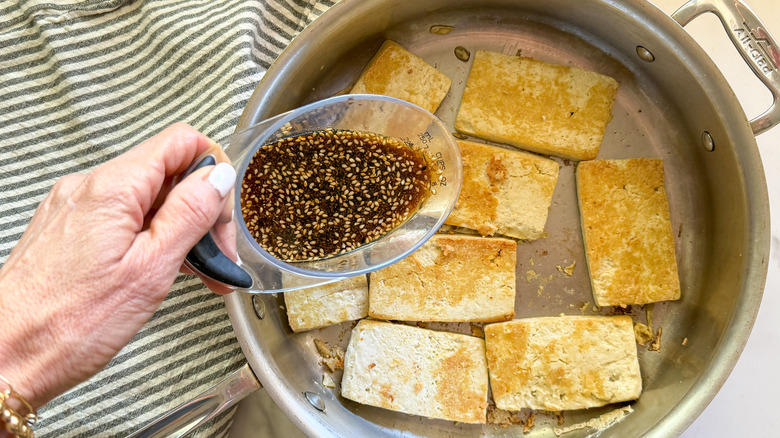 adding sauce to the pan of tofu