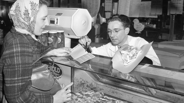 Woman using ration book to buy meat from a butcher during WWII